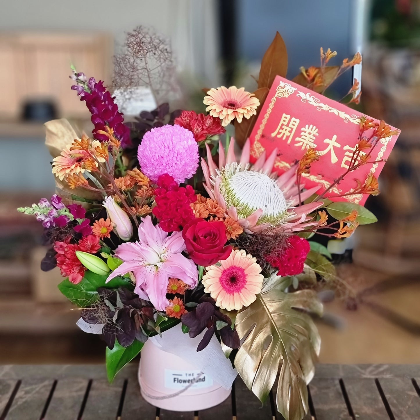 Vibrant Grand Opening Flower Hatbox with fresh seasonal blooms in reds and pinks including roses, protea and banksia | Celebration flower arrangement in signature hatbox | Flowerland Nunawading