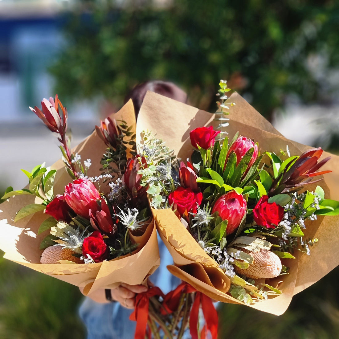 A premium Australian native flower arrangement featuring pink proteas and red roses wrapped in natural kraft paper, designed for residential homes in Rowville.