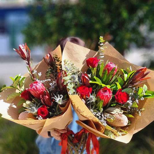 A premium Australian native flower arrangement featuring pink proteas and red roses wrapped in natural kraft paper, designed for residential homes in Rowville.