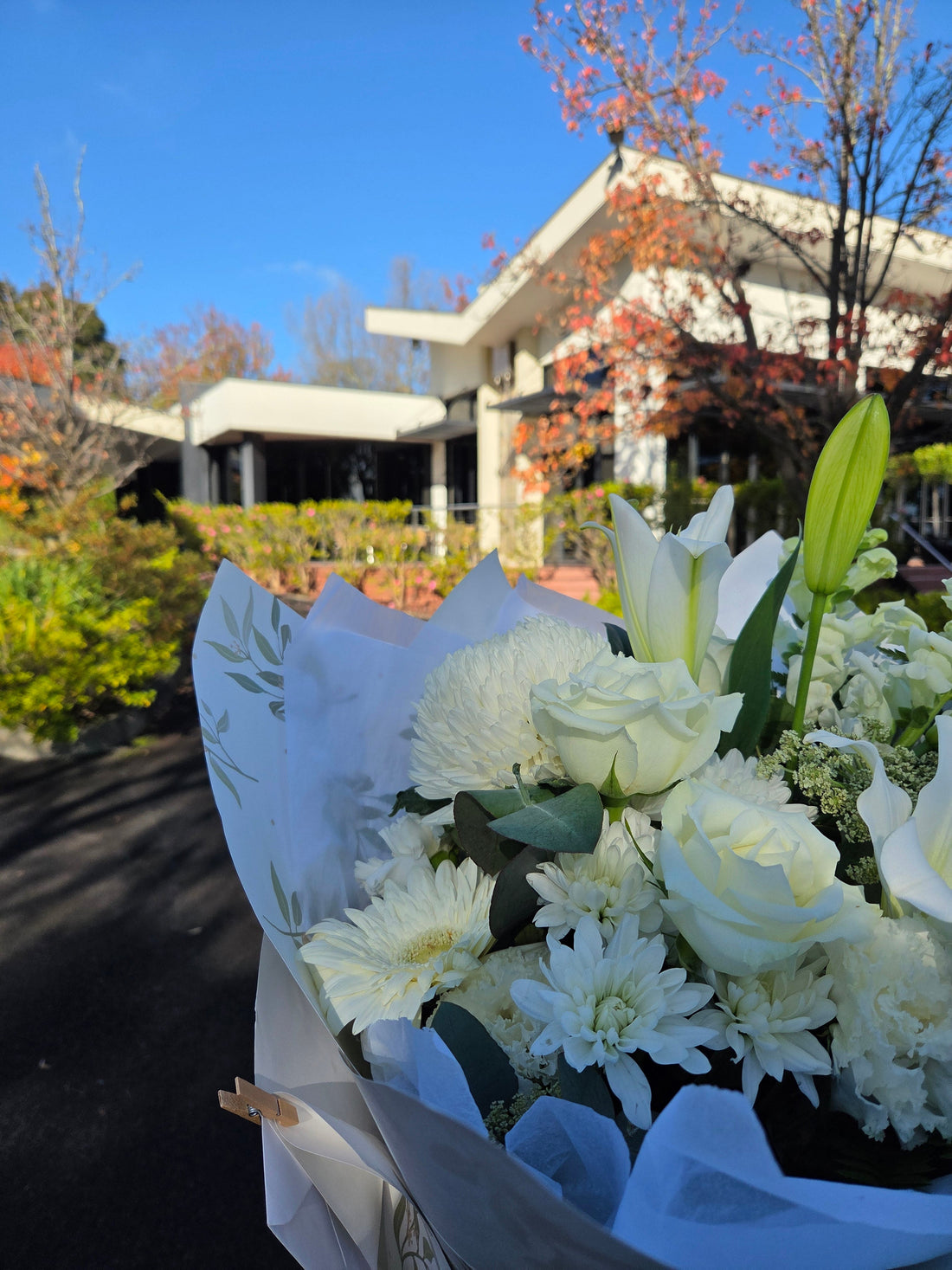 Funeral flower delivery in Ringwood featuring elegant white roses and lilies outside a modern local venue.