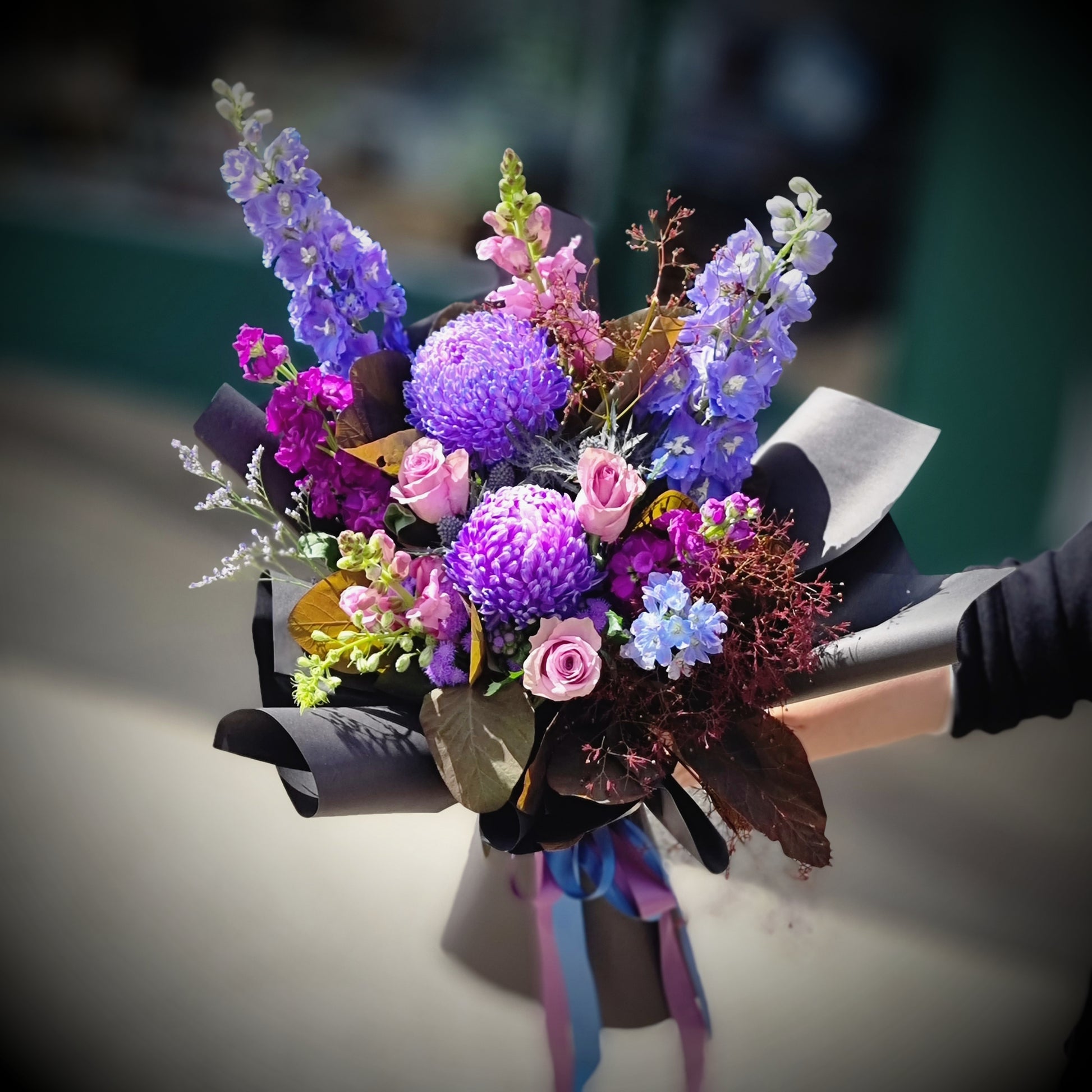 A stunning moody bouquet with blue delphiniums and purple carnations by The Flowerland.