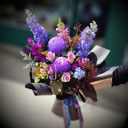 A stunning moody bouquet with blue delphiniums and purple carnations by The Flowerland.