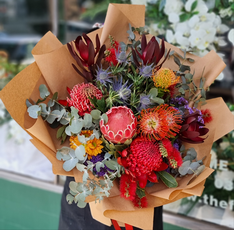Same-day flower delivery Box Hill - Premium native Australian bouquet featuring red protea, orange pincushion flowers, blue sea holly, and silver eucalyptus handcrafted by The Flowerland.