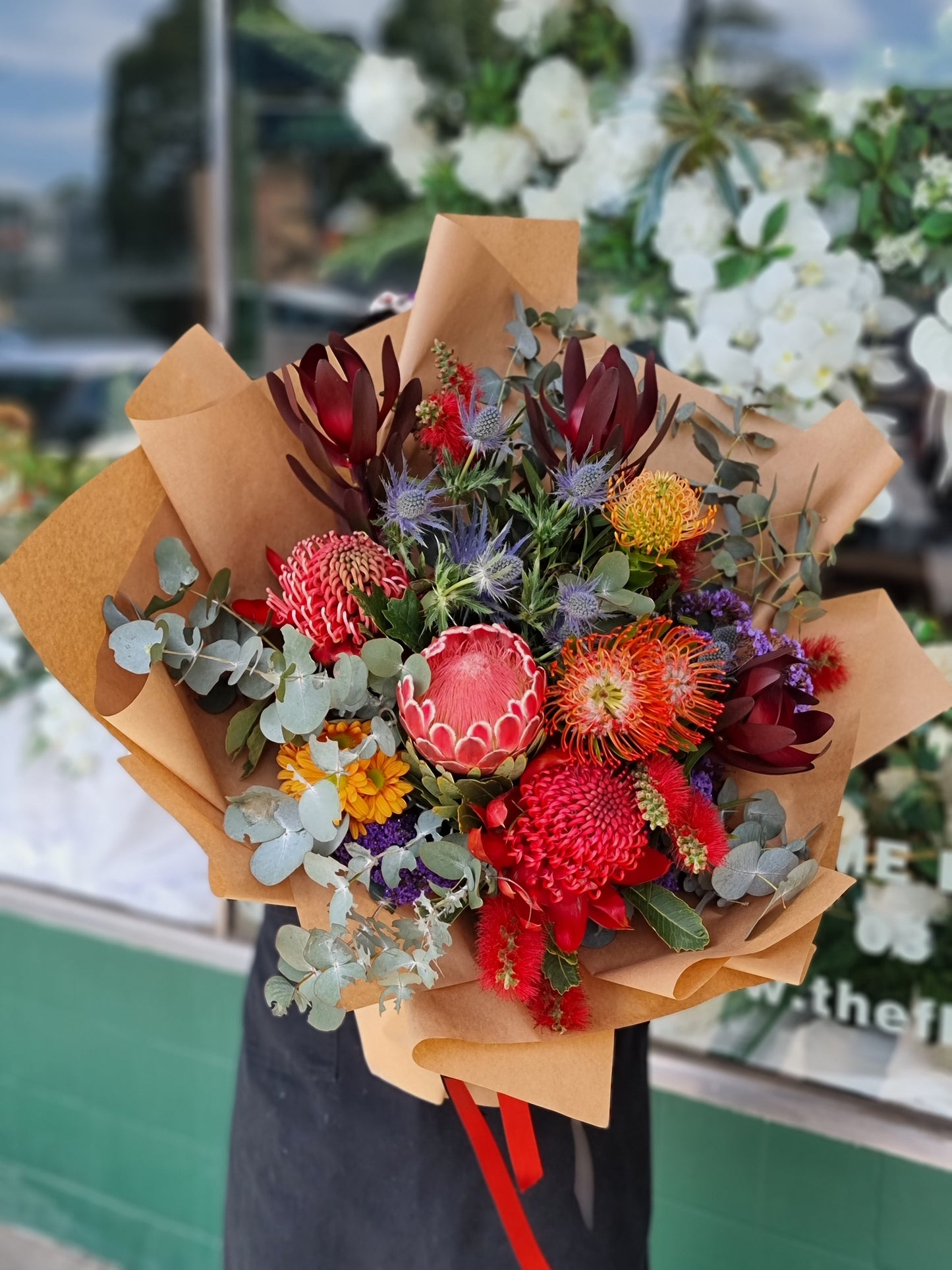 Same-day flower delivery Bulleen - Premium native Australian bouquet featuring red protea, orange pincushion flowers, blue sea holly, and silver eucalyptus handcrafted by The Flowerland.
