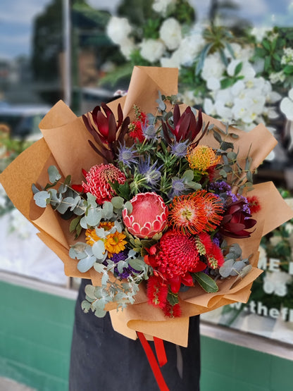 Same-day flower delivery Bulleen - Premium native Australian bouquet featuring red protea, orange pincushion flowers, blue sea holly, and silver eucalyptus handcrafted by The Flowerland.