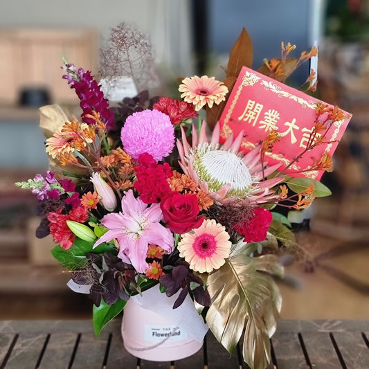 Vibrant Grand Opening Flower Hatbox with fresh seasonal blooms in reds and pinks including roses, protea and banksia | Celebration flower arrangement in signature hatbox | Flowerland Nunawading