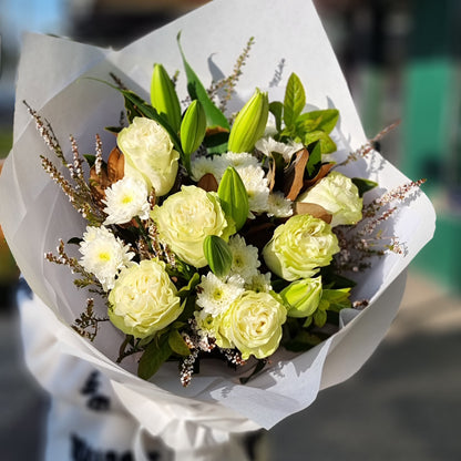 A premium hand-tied bouquet of fresh white roses, white lilies, and small white flowers with dark green leaves, finished with a precise white paper wrap. Reliable flower delivery across Melbourne's eastern suburbs.