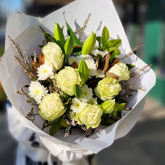 A premium hand-tied bouquet of fresh white roses, white lilies, and small white flowers with dark green leaves, finished with a precise white paper wrap. Reliable flower delivery across Melbourne's eastern suburbs.